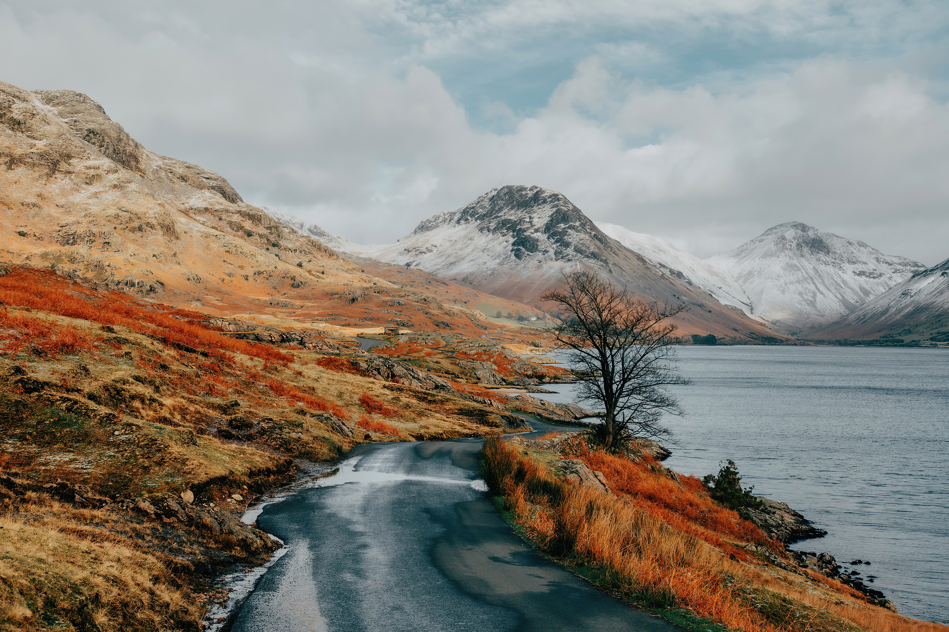 Winding road by a lake with snow-capped mountains HD Wallpaper