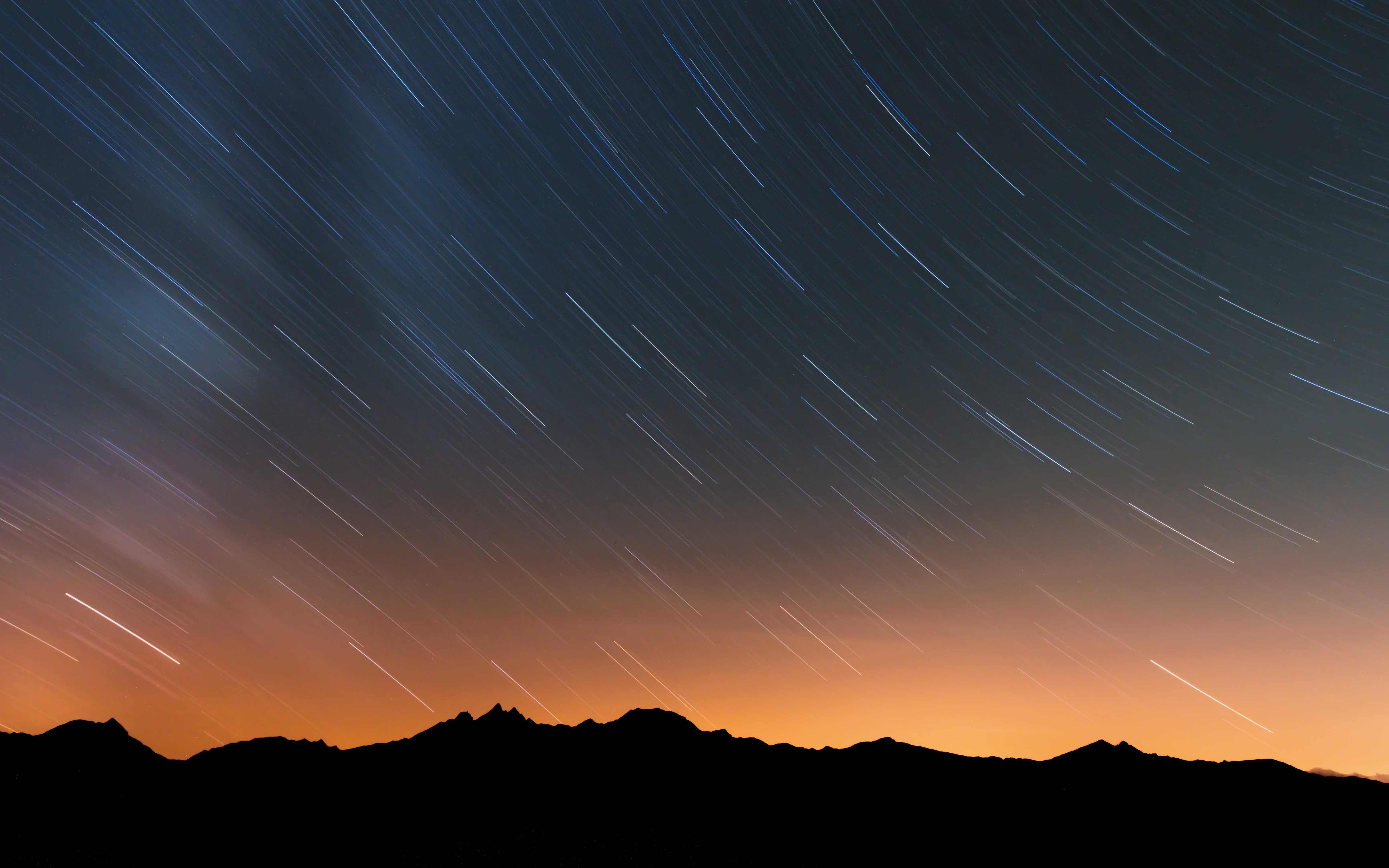 Star trails over silhouetted mountains at night HD Wallpaper