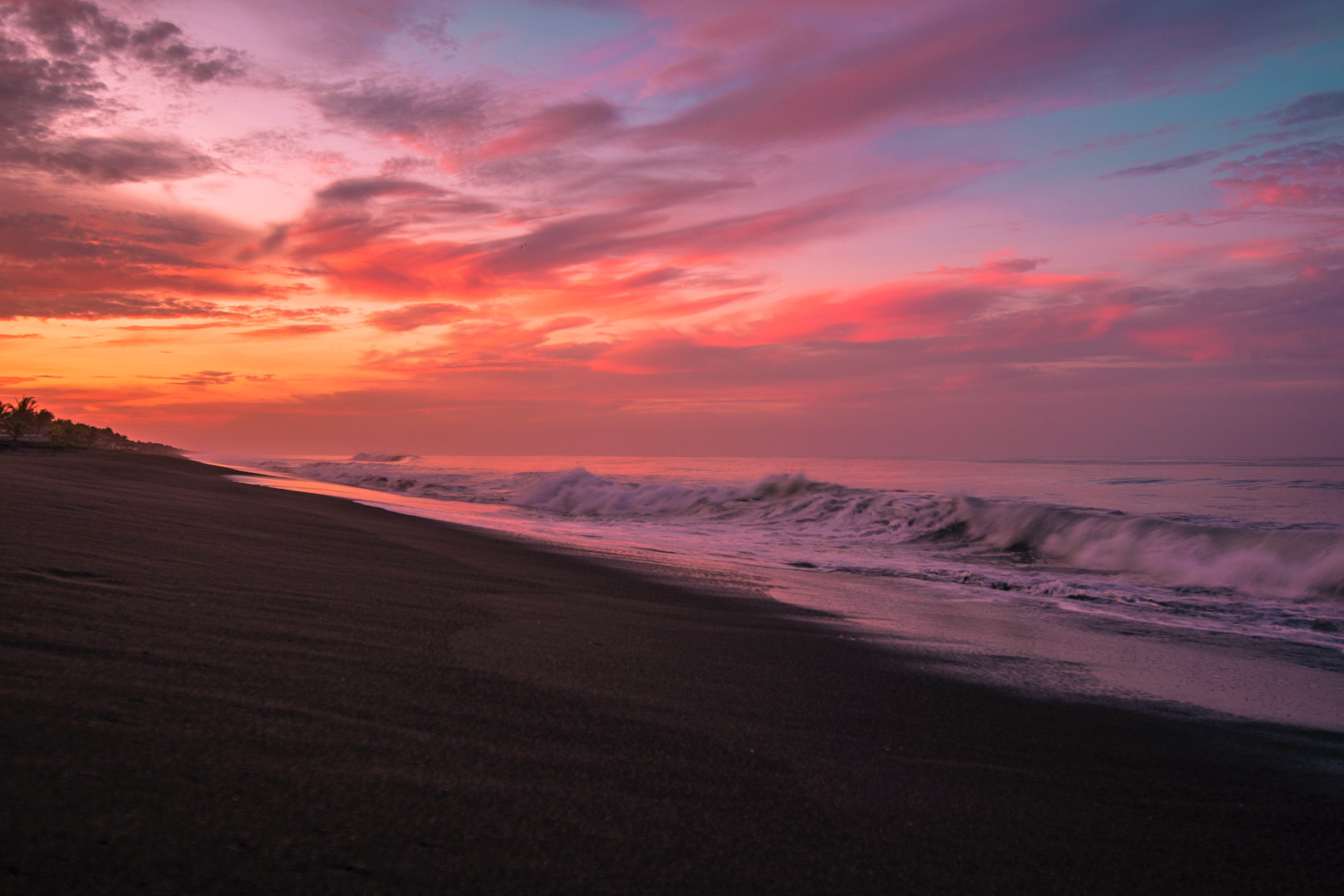Sunset over a dark sand beach with waves HD Wallpaper