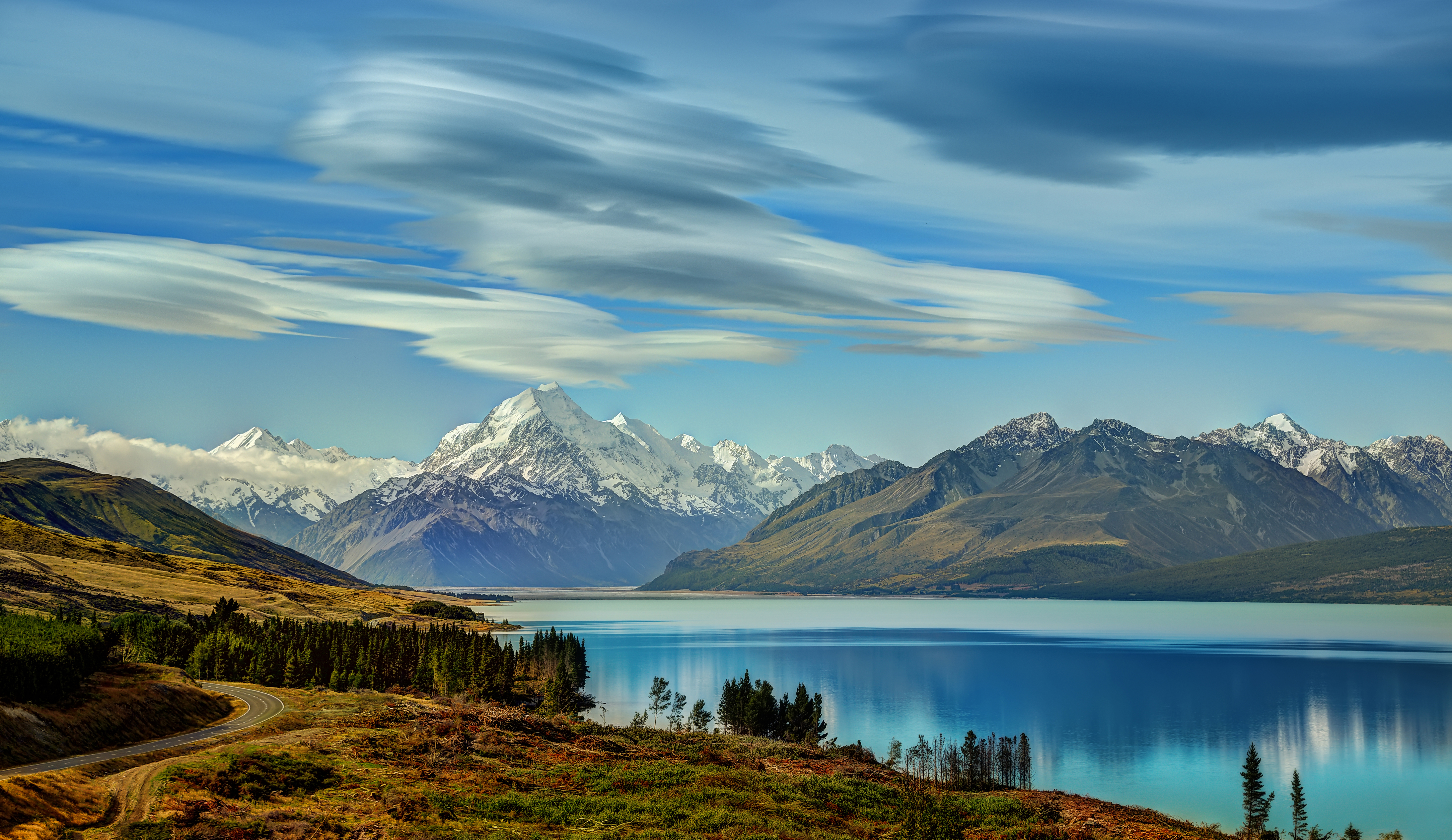 Snow-capped mountains reflected in a lake under a cloudy sky HD Wallpaper