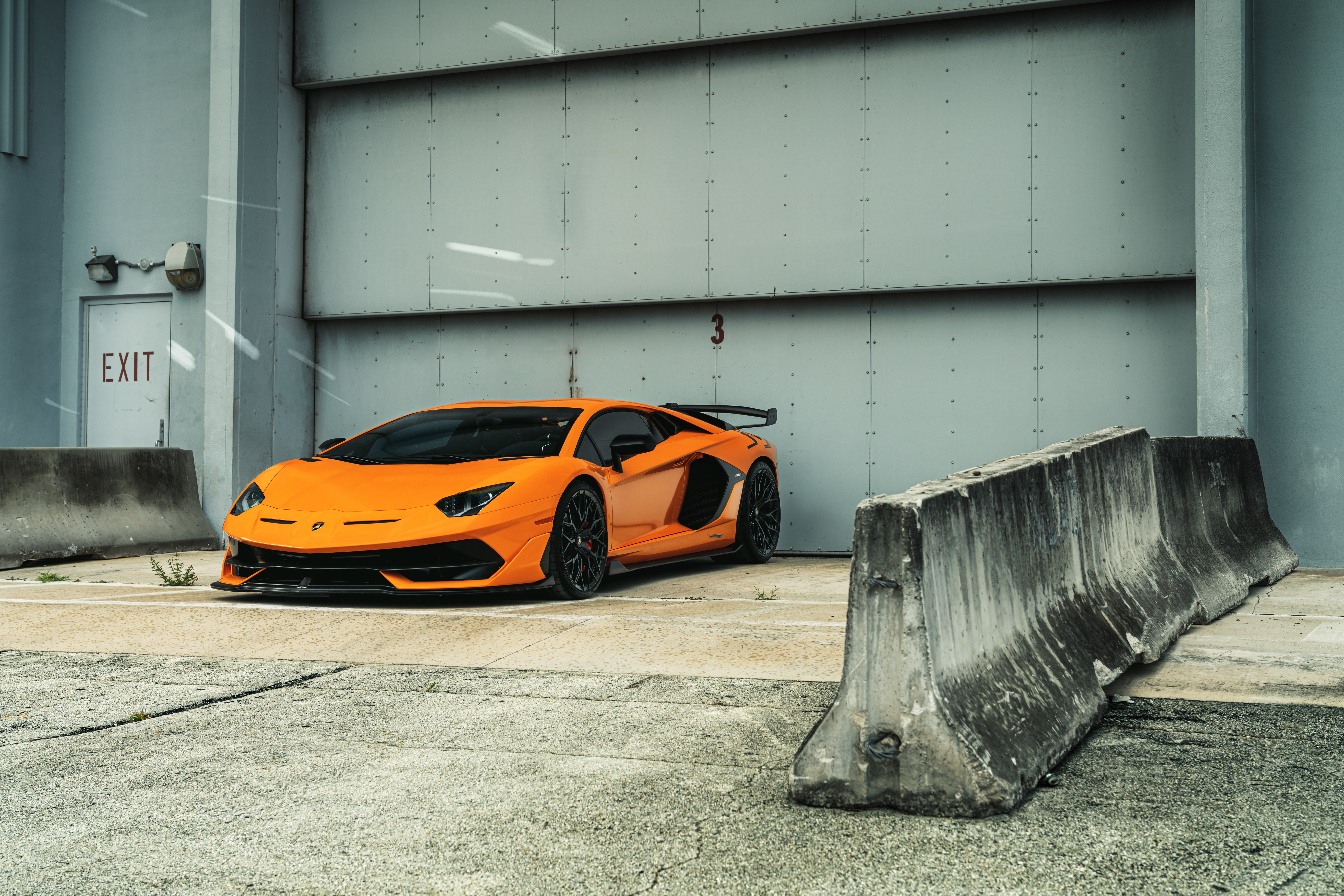 Orange Lamborghini Aventador SVJ parked near a large garage door HD Wallpaper