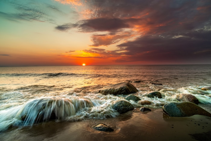 Sunset over the ocean with waves crashing on rocks