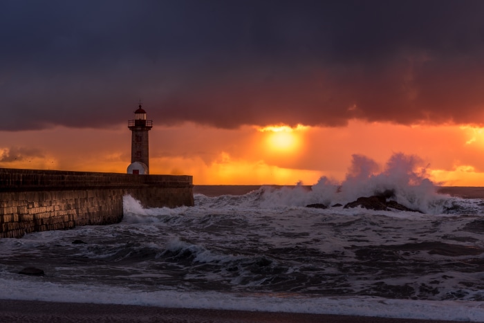 Lighthouse at sunset with crashing waves