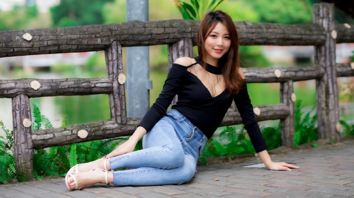 Asian Woman in Black Top and Jeans Sitting by Fence
