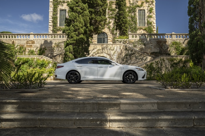 White Lexus ES 300h F SPORT parked near a stone building