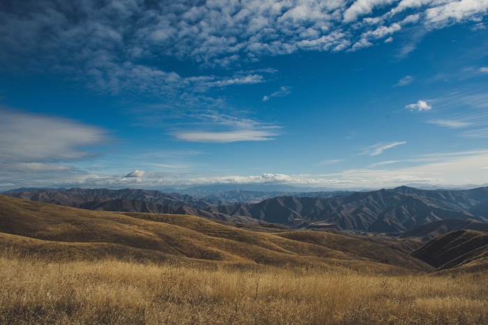 Golden hills and mountains under a blue sky with clouds