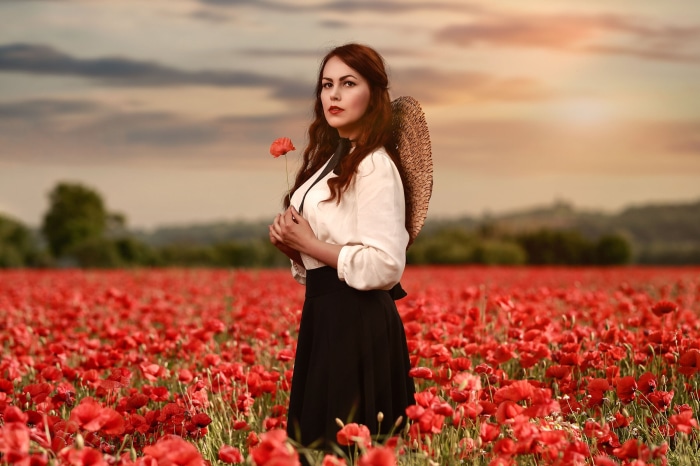 Woman in a poppy field holding a red poppy
