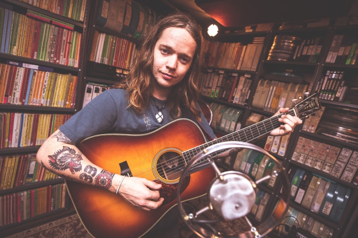Billy Strings playing guitar in front of bookshelves