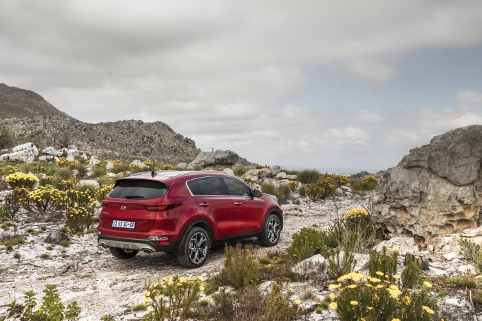 Red Kia Sportage SUV on a rocky, floral terrain