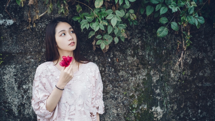 Asian woman holding a red flower near a stone wall