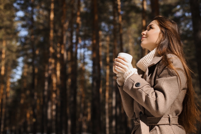 Brunette woman holding a mug in a forest