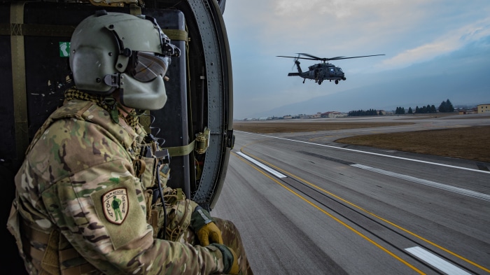 Soldier in helicopter watches another helicopter take off