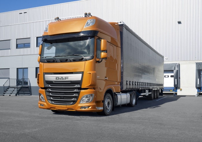 Orange DAF semi-truck parked at a warehouse