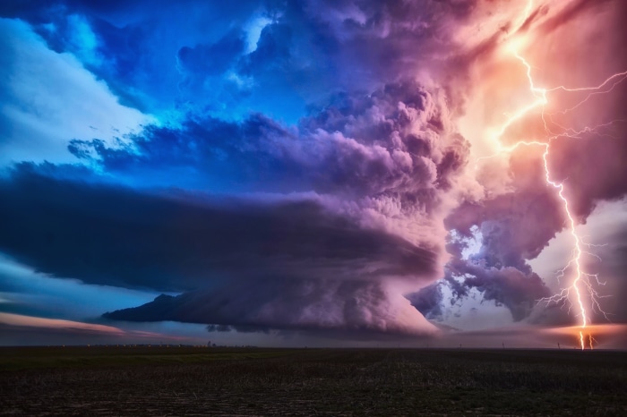 Lightning strikes a massive storm cloud over a field