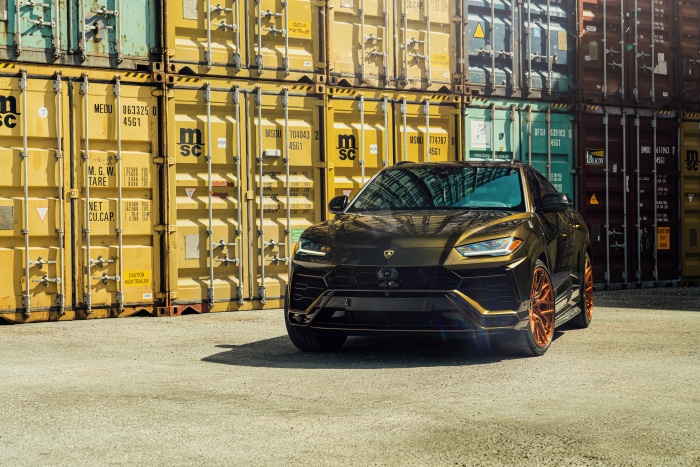 Gold Lamborghini Urus SUV parked by shipping containers