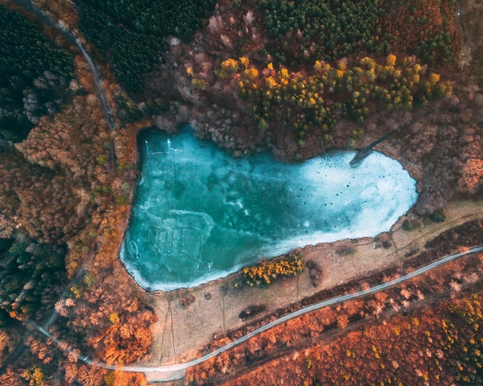Aerial view of a frozen lake surrounded by autumn forest in Hungary