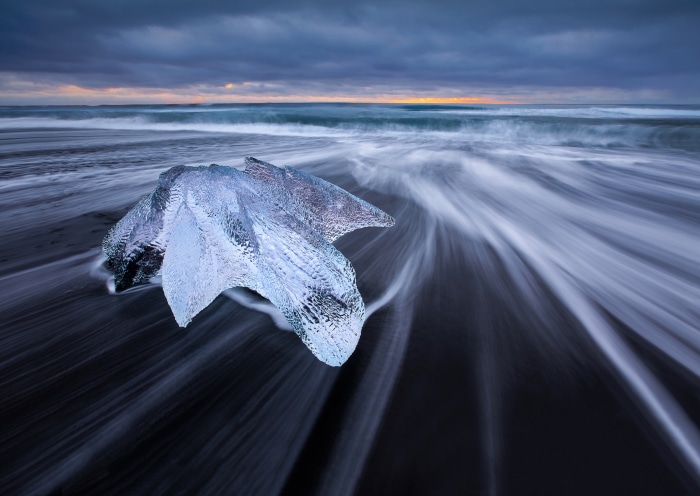Iceberg on a black sand beach with ocean waves