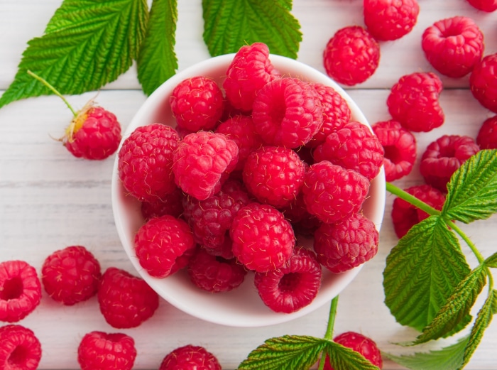 Raspberries in a white bowl with leaves
