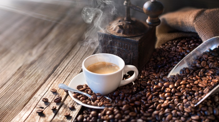 Steaming cup of coffee with coffee beans and grinder