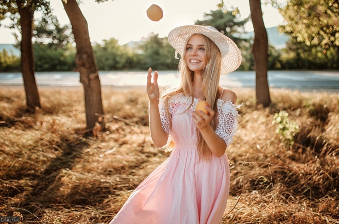 Young woman in pink dress juggling peaches outdoors