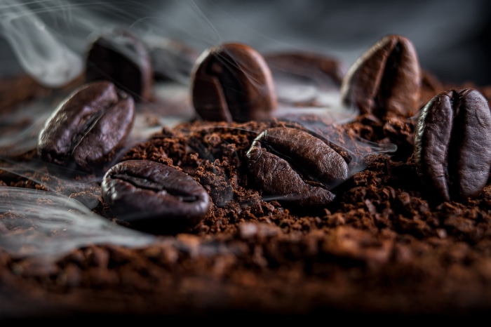 Macro shot of steaming coffee beans on ground coffee