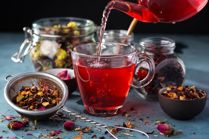 Tea being poured into a glass cup with dried tea leaves