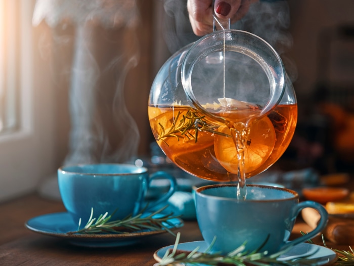 Tea being poured from a glass kettle into a blue cup