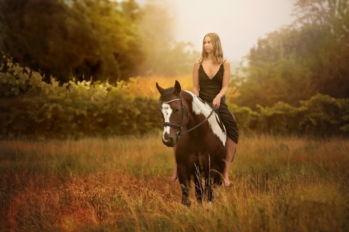 Woman in black dress riding a horse in a field