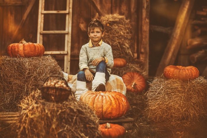 Boy sitting on hay bales with pumpkins