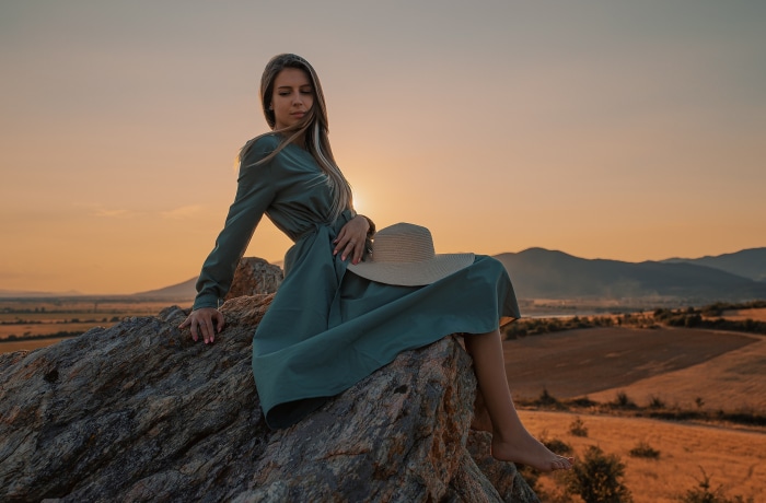 Woman in dress sitting on rock with hat
