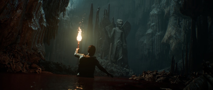 Man with torch in cave with statue and bones