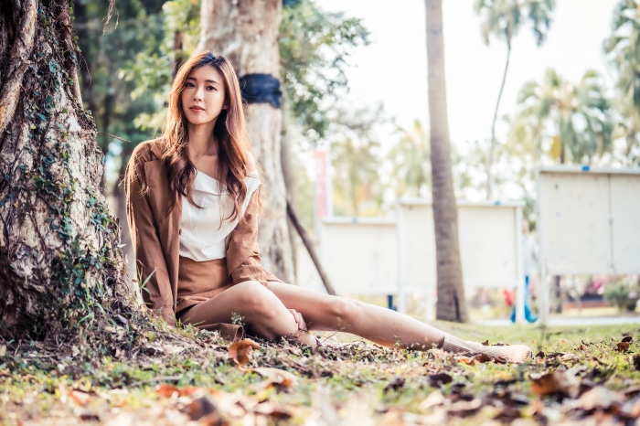 Asian woman with brunette hair sitting by a tree
