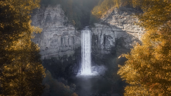 Waterfall cascading down a rocky cliff face surrounded by autumn trees