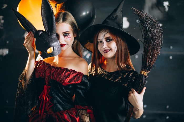 Two women in Halloween costumes with masks and broom