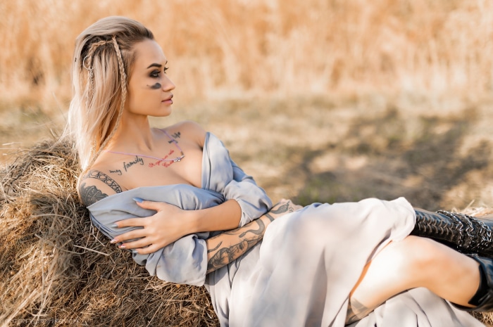 Woman with tattoos lying on hay bale