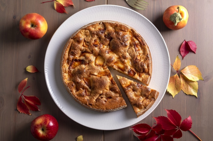 Apple pie on a white plate with apples and autumn leaves