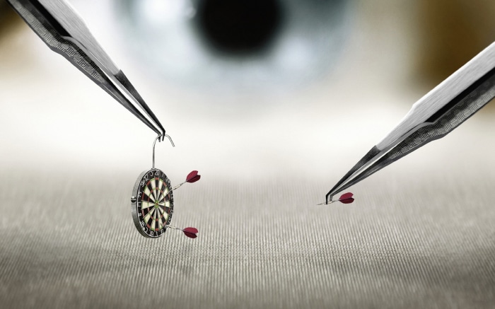 Miniature darts and dartboard held by tweezers