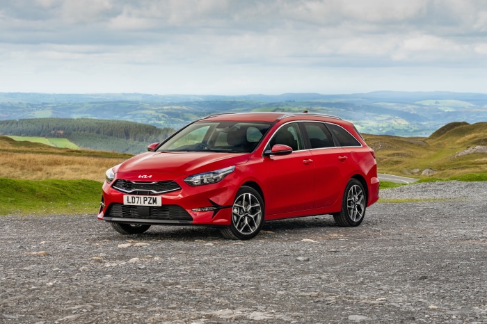 Red Kia Ceed Sportswagon parked on gravel with hills background