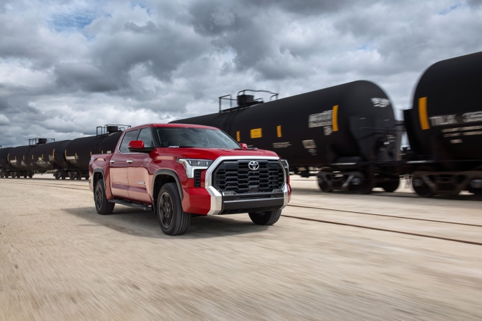 Red Toyota Tundra driving next to a train