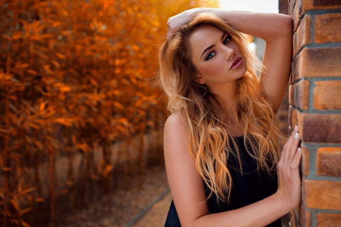 Woman with blonde hair leaning against a brick wall