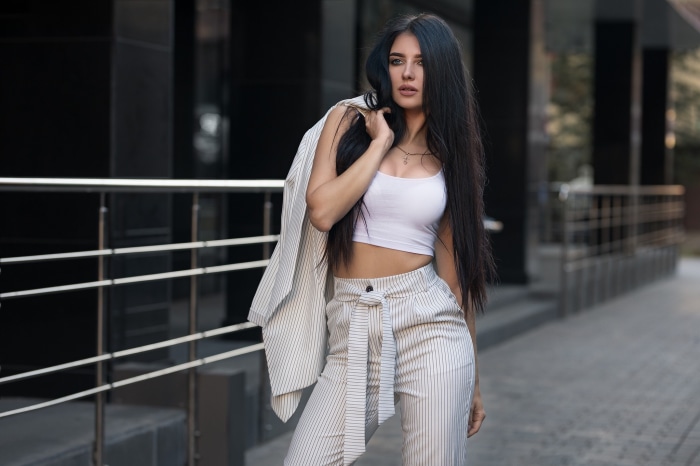 Woman with black hair wearing a white crop top and striped suit