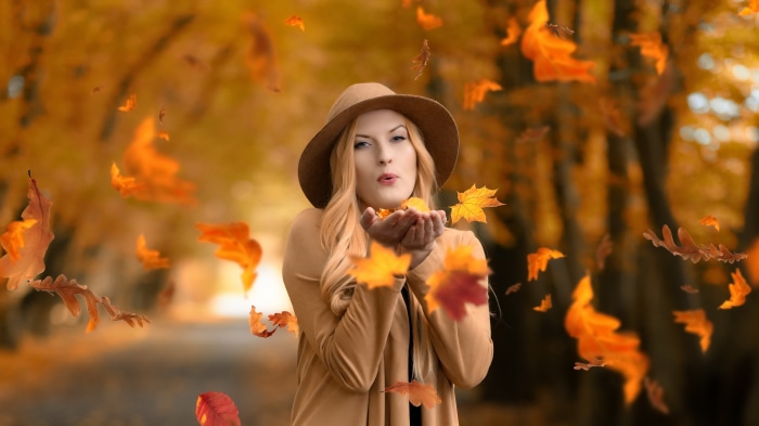 Woman in hat blowing autumn leaves