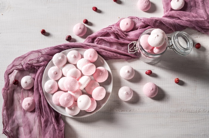 Pink meringues with cranberries on a white wooden table
