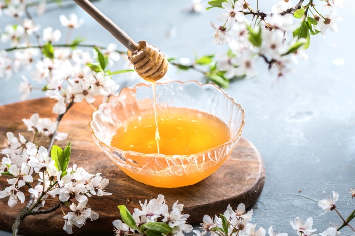 Honey dripping from a dipper into a bowl with flowers