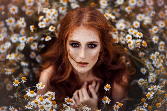 Redhead woman with freckles surrounded by daisies