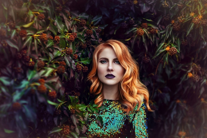 Redhead woman with dark lipstick in front of foliage