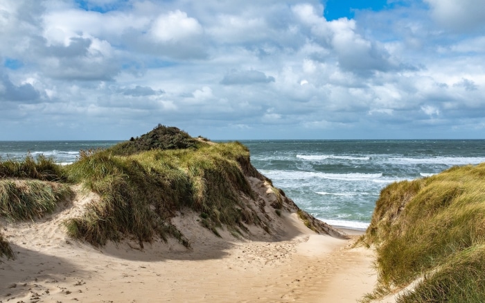 Sandy dunes and ocean waves under a cloudy sky
