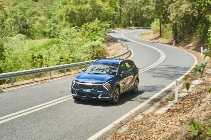 Blue Kia Sportage driving on a winding road