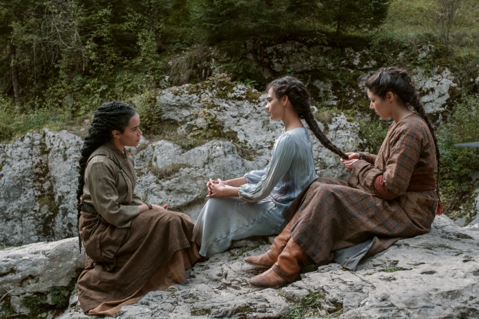Three women braiding hair in a forest