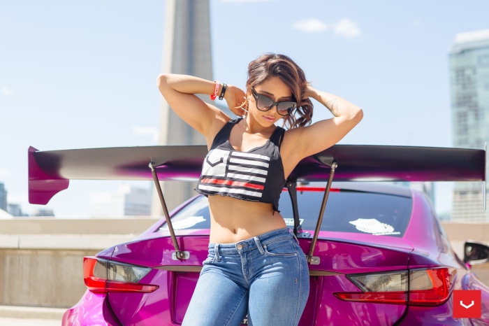 Woman in crop top and jeans posing by a custom car